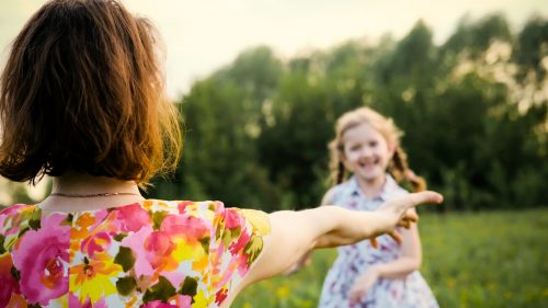 A little daughter hugs her mother's shoulders outdoors. Nature. Mom and her child play together in the park