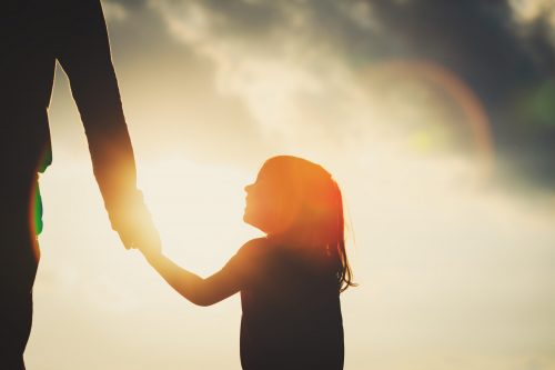 silhouette of little girl holding parent hand at sunset